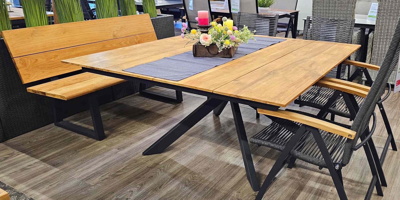 Ein moderner Esstisch aus Holz mit einer eleganten Tischdecke und einem Blumengesteck, umgeben von bankartigen und klappbaren Stühlen in einem stilvollen Innenraum.